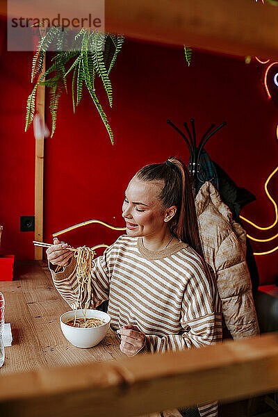 Lächelnde Frau isst Ramen im Restaurant