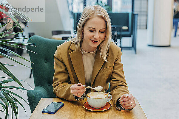 Lächelnde Frau mit blonden Haaren beim Kaffee im Café