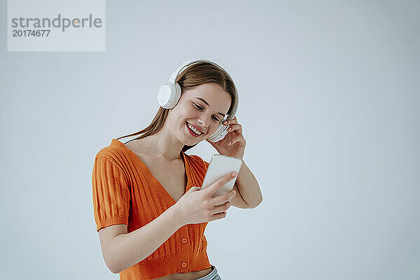 Lächelnde Frau mit kabellosen Kopfhörern und Smartphone vor weißem Hintergrund