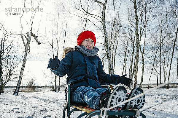 Fröhlicher Junge sitzt im Winter auf Schlitten