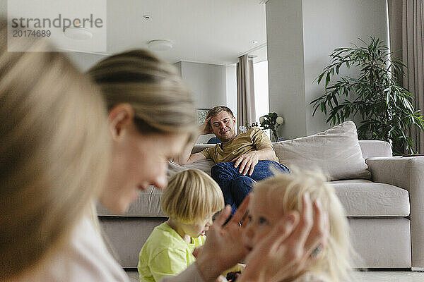Glücklicher Mann blickt Familie im heimischen Wohnzimmer an