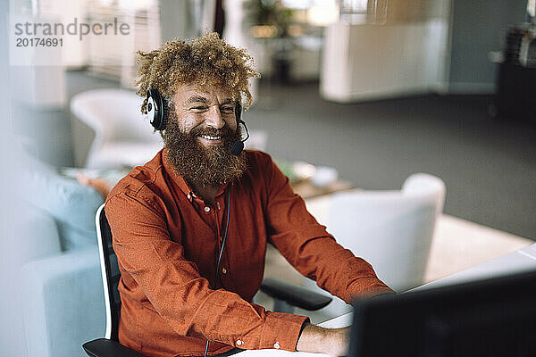 Glücklicher Geschäftsmann  der ein Headset trägt und im Büro am Computer arbeitet