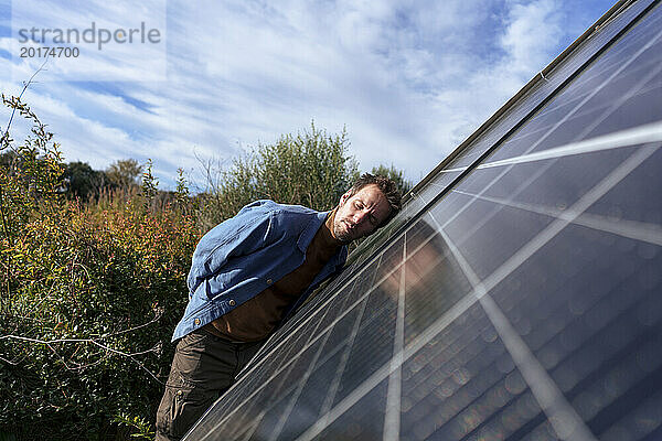Mann stützt sich an einem sonnigen Tag mit geschlossenen Augen auf ein Solarpanel