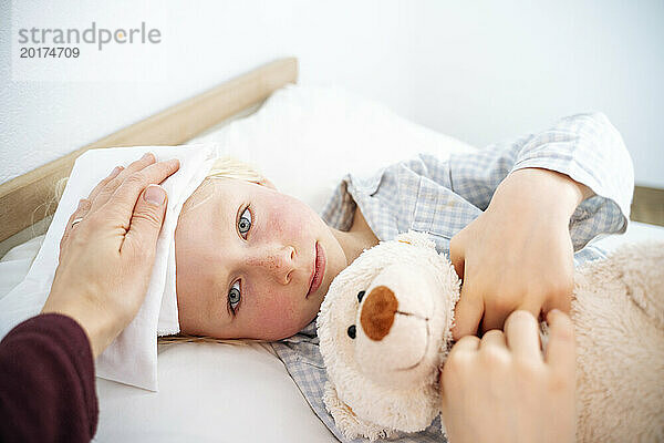 Mutter kümmert sich um ihren kranken Sohn  der zu Hause mit Teddybär im Bett liegt