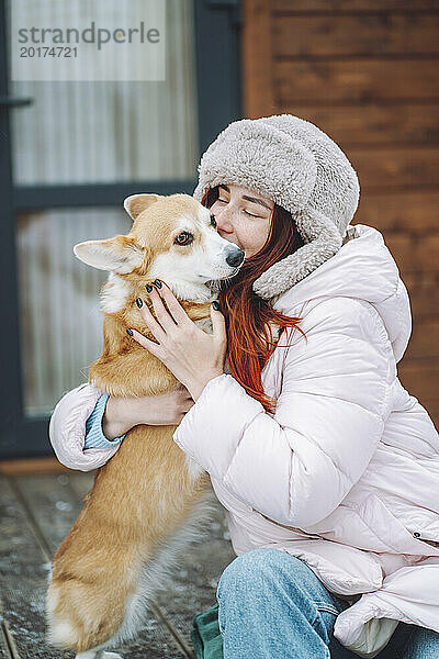 Junge Frau küsst Corgi-Hund auf der Veranda