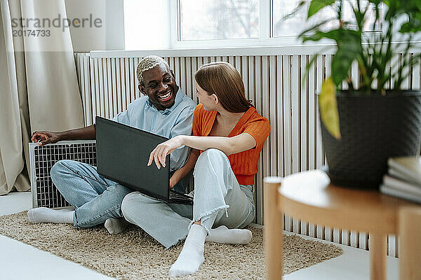 Fröhliche Männer und Frauen sitzen mit Laptop am Fenster zu Hause