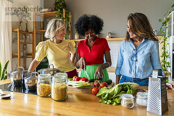Frau schneidet Gemüse mit Freunden in der heimischen Küche