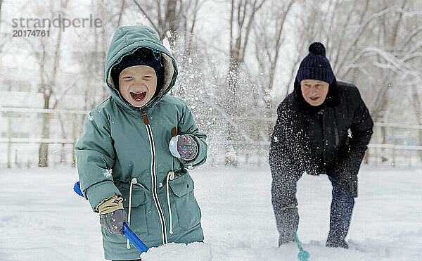 Fröhlicher Junge spielt mit Großvater im Schnee im Park