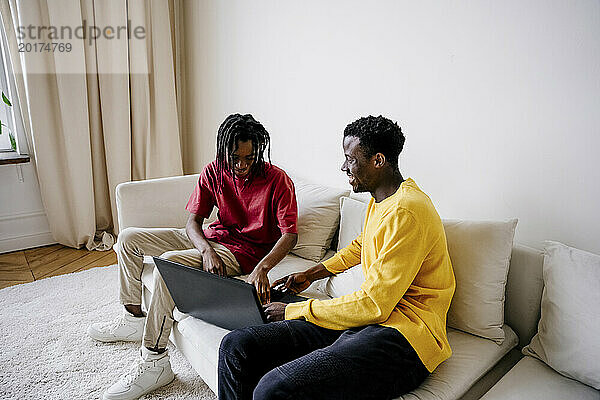 Glückliche Freunde  die zu Hause einen Laptop auf dem Sofa benutzen