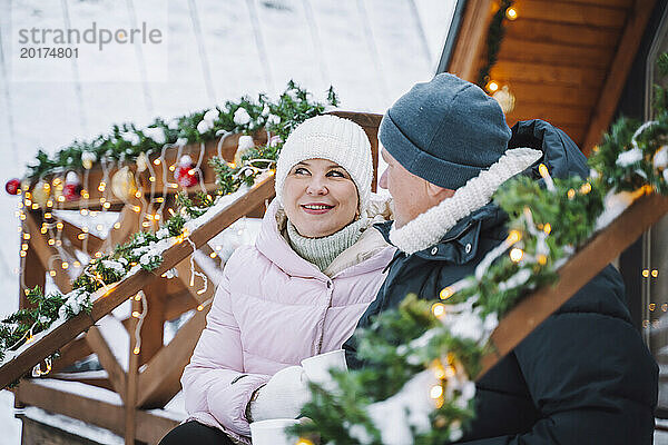 Lächelnde Frau mit Mann in warmer Kleidung in der Nähe einer Blockhütte