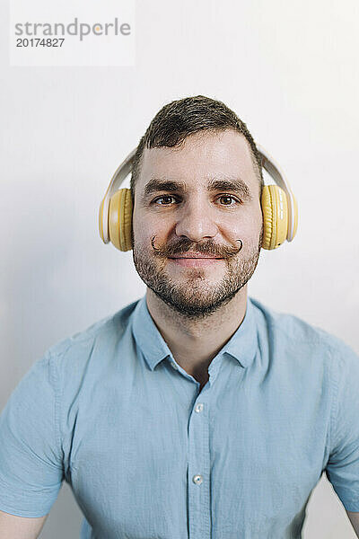 Lächelnder Mann mit kabellosen Kopfhörern  der vor der Wand Musik hört