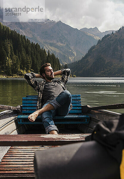 Junger Mann entspannt sich an einem sonnigen Tag im Boot am Vilsalpsee in der Nähe von Bergen  Tirol  Österreich