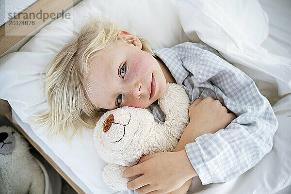 Lächelnder Junge umarmt Teddybär zu Hause im Bett