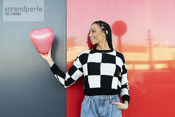 Glückliche junge Frau hält Luftballon vor der Wand