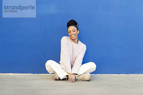 Fröhliche junge Frau sitzt vor einer blauen Wand