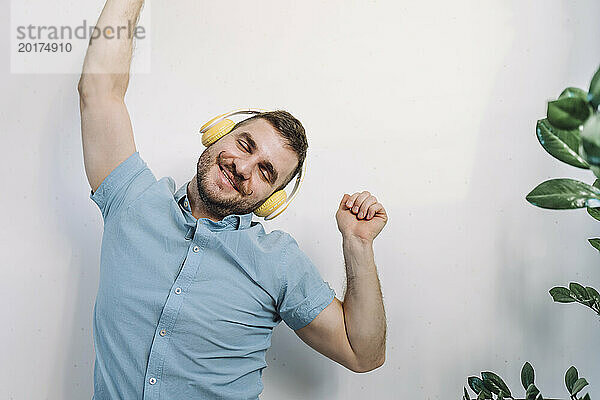 Fröhlicher Mann  der über kabellose Kopfhörer Musik hört und zu Hause tanzt