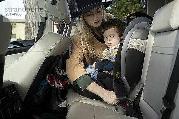 Mutter passt Sicherheitsgurt für Sohn an  der im Auto sitzt