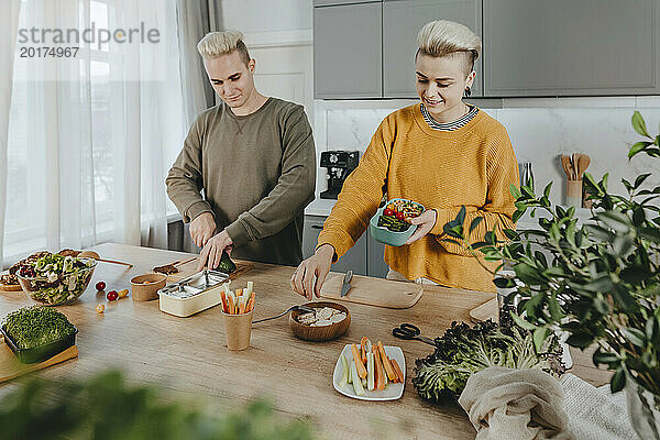 Glückliches Paar bereitet zu Hause in der Küche gesundes Essen für Lunchboxen zu