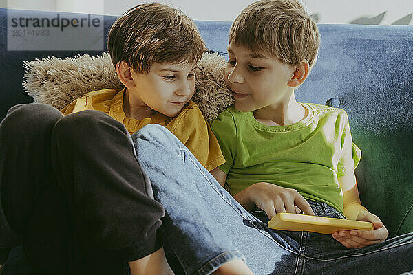 Geschwister teilen sich ihr Smartphone und sitzen zu Hause auf dem Sofa