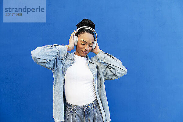 Glückliche Frau mit kabellosen Kopfhörern vor blauer Wand