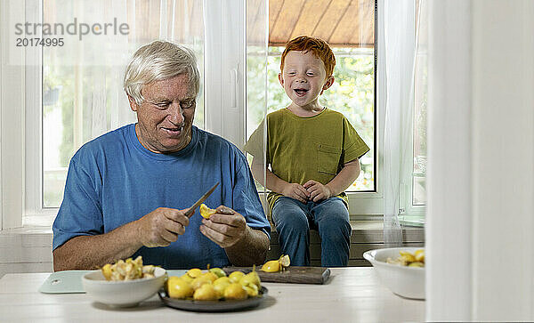 Glücklicher Junge sitzt neben Großvater und schneidet zu Hause Früchte