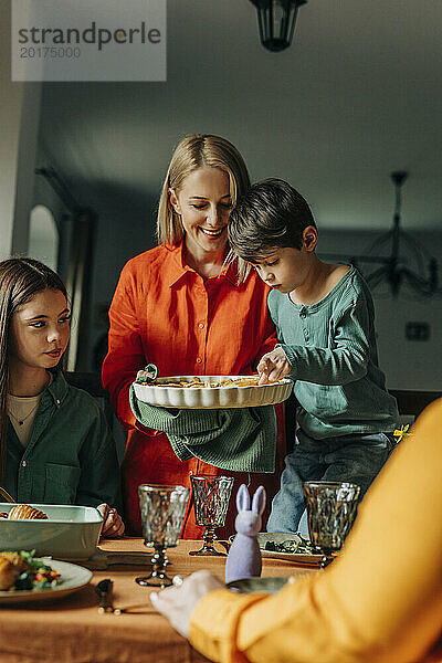 Boy having savory pie by mother standing near dining table at Easter dinner