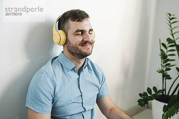 Lächelnder Mann mit geschlossenen Augen  kabellosen Kopfhörern und Musikhören