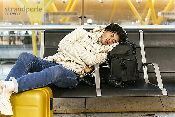 Junger Mann macht ein Nickerchen und stützt sich auf einen Rucksack in der Flughafenlounge