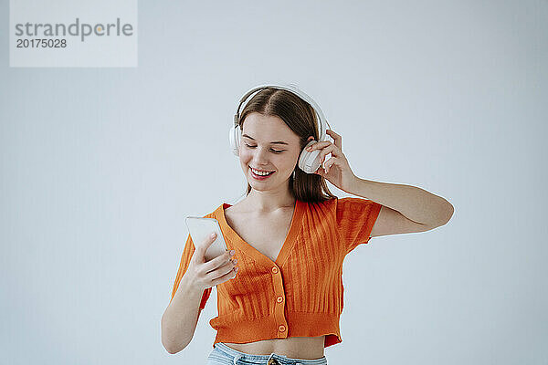 Junge Frau trägt kabellose Kopfhörer und hört Musik vor weißem Hintergrund
