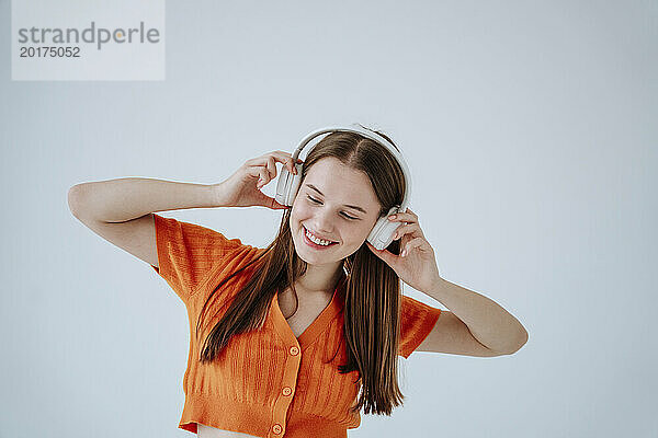 Smiling woman with eyes closed listening to music against white background