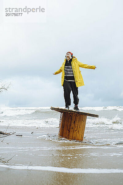 Sorglose Frau steht auf einer Holzspule am Strand