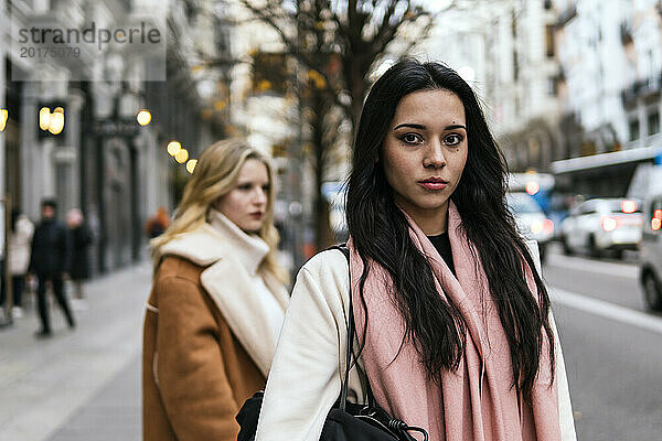 Junge Frau mit Freundin steht im Hintergrund auf der Straße