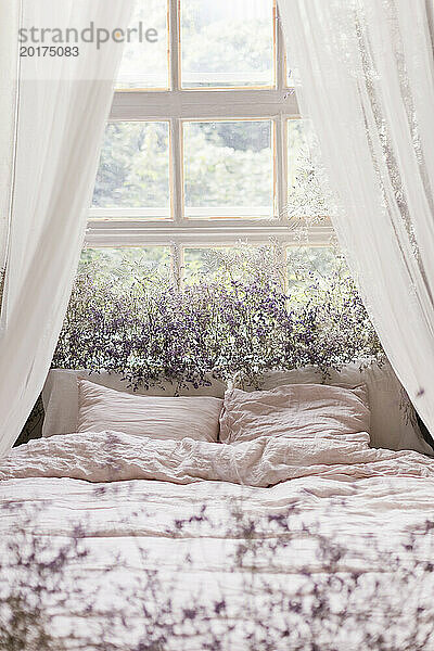 Bett am Fenster mit Trockenblumen geschmückt