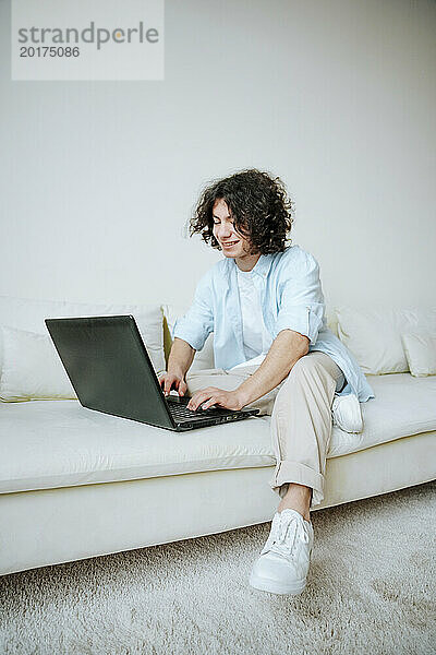 Glücklicher junger Mann  der zu Hause auf dem Sofa einen Laptop benutzt