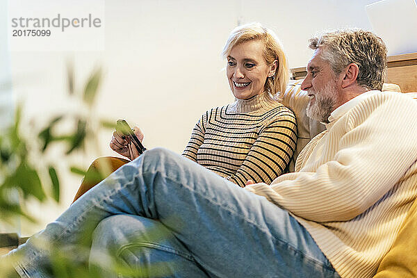 Lächelnde Frau zeigt Mann zu Hause Smartphone