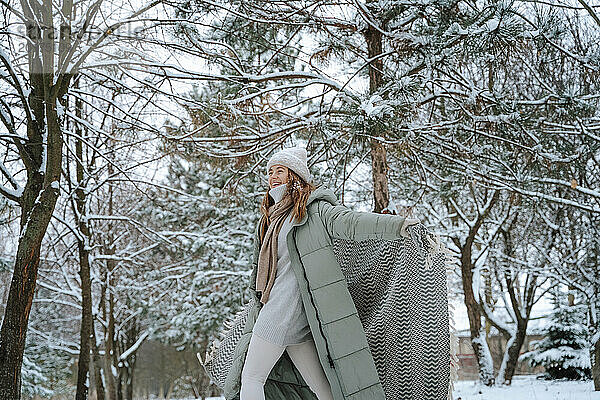 Glückliche Frau  die im Winter mit einer Decke im Schnee spielt