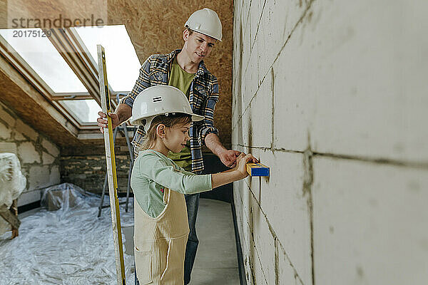Vater und Tochter benutzen Nivelliergerät an der Wand in einem Zimmer  das gerade renoviert wird