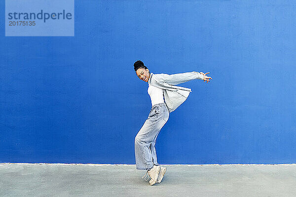 Glückliche junge Frau tanzt vor einer blauen Wand