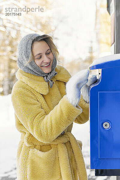 Glückliche junge Frau steckt Postkarte in Briefkasten