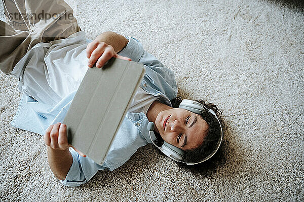 Mann liegt auf Teppich und benutzt Tablet-PC zu Hause