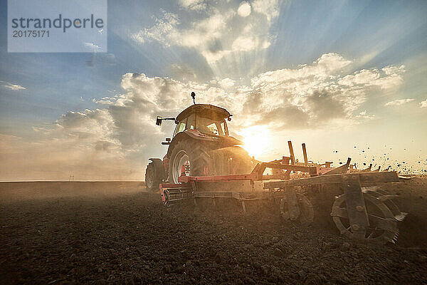 Traktor pflügt Feld bei Sonnenuntergang