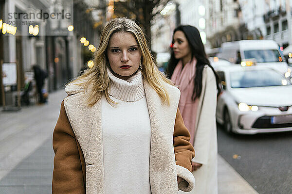 Selbstbewusste junge Frau trägt Mantel und steht auf der Straße in der Stadt