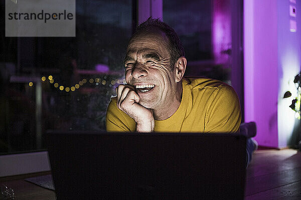 Reifer Mann lacht zu Hause neben Laptop
