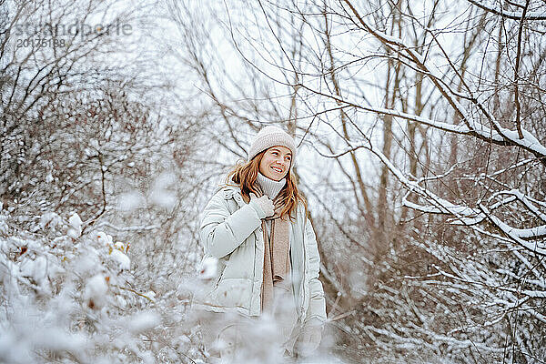 Lächelnde Frau verbringt im Winter ihre Freizeit inmitten gefrorener Bäume