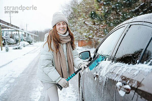 Lächelnde Frau putzt Auto im Winter mit Besen