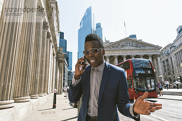 Reifer Geschäftsmann gestikuliert und spricht mit dem Smartphone in der Londoner Innenstadt