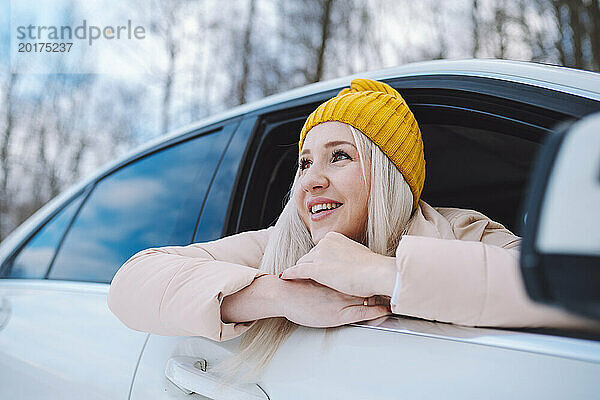 Glückliche Frau lehnt sich im Winterwald aus dem Autofenster
