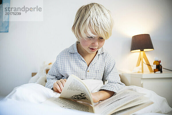 Blonder Junge liest zu Hause im Bett ein Buch