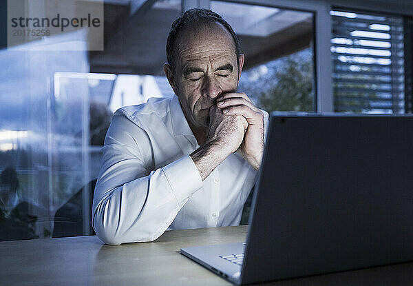 Reifer Freiberufler macht im Heimbüro neben dem Laptop ein Nickerchen