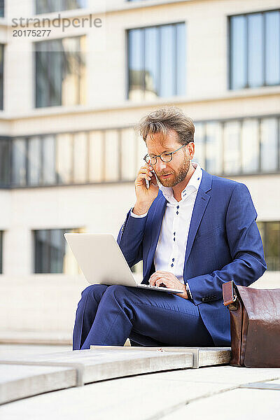 Geschäftsmann arbeitet am Laptop und spricht über Smartphone in der Stadt